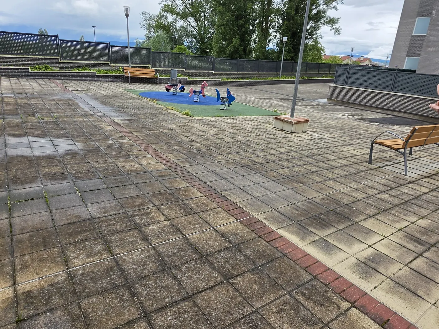 Zona común amplia de urbanización con suelo de adoquines y zona infantil tras limpieza